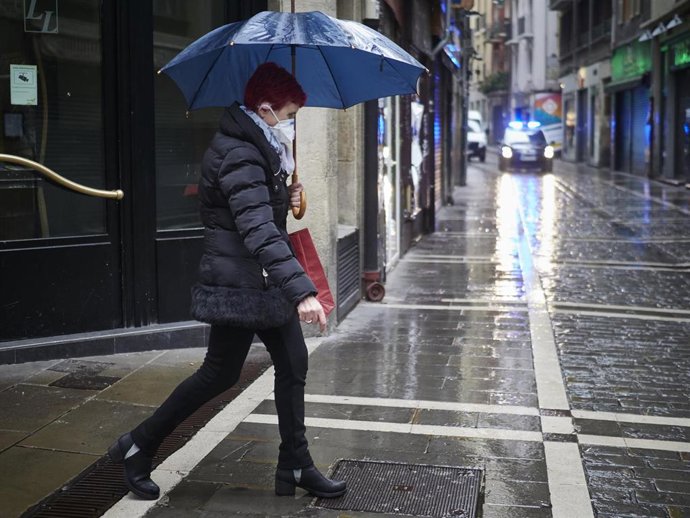 Archivo - Una mujer con mascarilla camina protegiéndose con un paraguas por la lluvia por el casco viejo de Pamplona durante el Martes Santo y la cuarta semana del estado de alarma decretado por el Gobierno por la crisis del coronavirus, en Pamplona/Nav