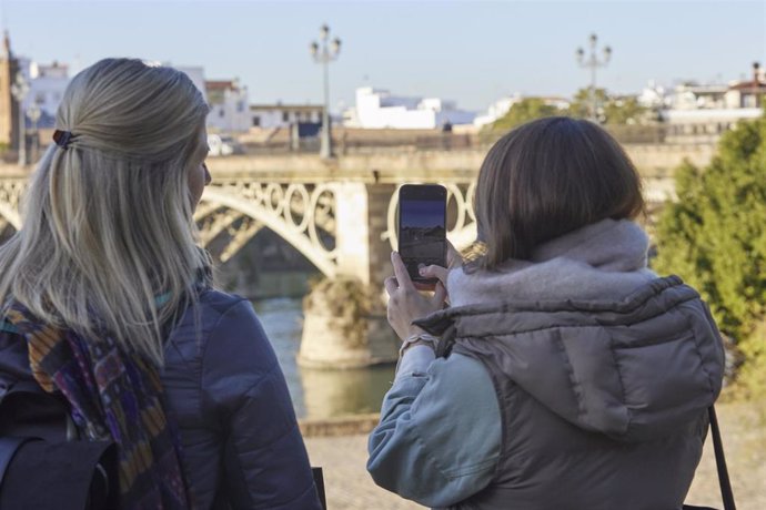 Archivo - Dos turistas fotografían el puente de Triana (foto de archivo)