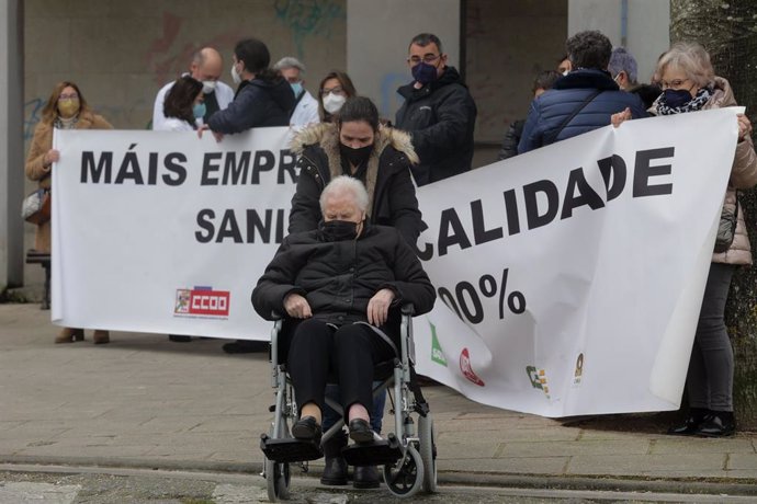 Una mujer en silla de ruedas pasa por delante de varios sanitarios que protestan, con una pancarta que reza 'Más empleo y de más calidad. Sanidad Pública 100%'