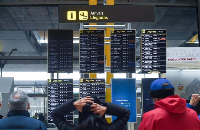 Archivo - Varias personas observan los paneles de llegadas en el aeropuerto de Adolfo Suárez, un día previo a la Nochebuena, a 23 de diciembre de 2021, en Madrid (España).