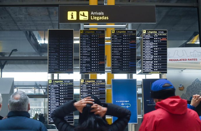 Archivo - Varias personas observan los paneles de llegadas en el aeropuerto de Adolfo Suárez, un día previo a la Nochebuena, a 23 de diciembre de 2021, en Madrid (España). Iberia opera el 100% de su red global previa a la pandemia durante estas fechas n