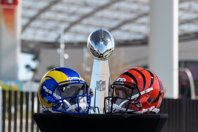 09 February 2022, US, Inglewood: The helmets of Super Bowl participants Los Angeles Rams (L) and Cinncinati Bengals stand on a table in front of the Vince Lombardy Trophy, which the winner receives, ahead of Commissioner of the National Football League 