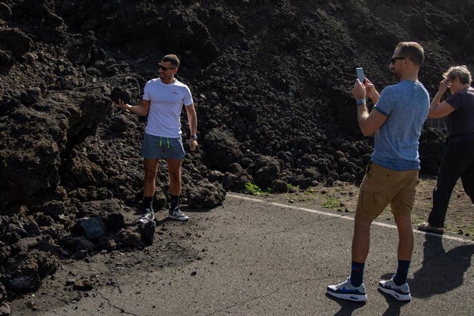 Un turista sostiene en la mano una piedra volcánica mientras otro le hace una fotografía en La Palma