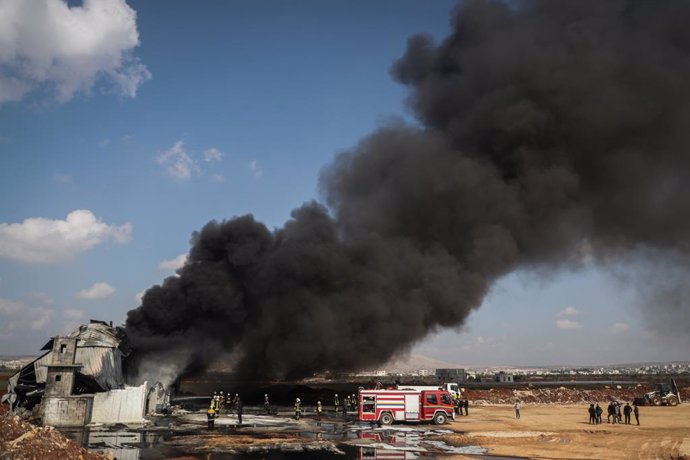 16 February 2022, Syria, Dana: Thick smoke rises as members of the Syria Civil Defence, known as White Helmets, put out a fire that broke out at a fuel depot as a result of a missile attack by the Syrian regime and Russian forces on Tarminin village nea