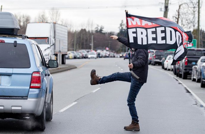 19 February 2027, Canada, Surrey: A person holding a "mandate freedom" flag kicks at the car of a reporter as they leave a rally against vaccine mandates at Hwy 15 and 8th ave in Surrey. Photo: Ryan Walter Wagner/ZUMA Press Wire Service/dpa
