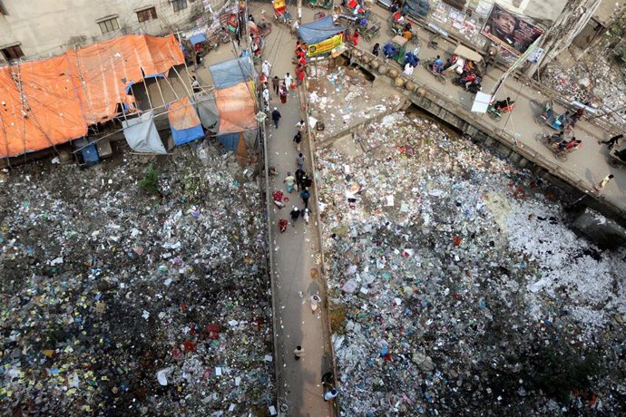 25 January 2022, Bangladesh, Dhaka: People walk along a bridge over a polluted area as plastic materials are collected. Photo: Habibur Rahman/ZUMA Wire/dpa