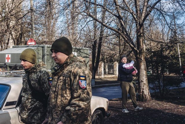 Unos soldados del ejército ucraniano caminan frente a un padre y su bebe, a 23 de febrero de 2022, en Chasiv Yar