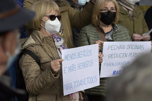 Dos mujeres sostienen unas pancartas en un acto simbólico de denuncia de la exclusión financiera en Galicia.