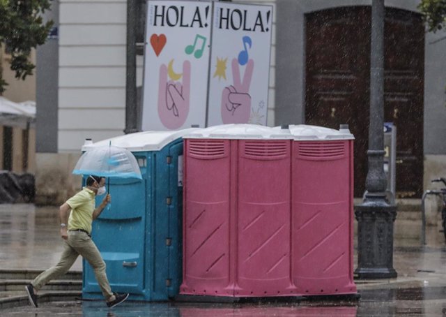 Archivo - Una persona corre con un paraguas frente a unos contenedores mientras llueve
