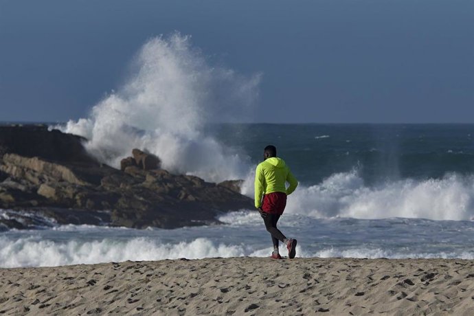 Una persona corre por la playa con intenso oleaje (archivo)