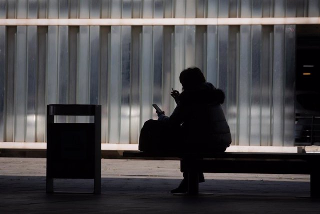 Archivo - Una mujer mira su teléfono móvil sentada en un banco en el Aeropuerto de Barcelona-El Prat, a 19 de noviembre de 2021, en El Prat de Llobregat, Barcelona, Catalunya (España). 