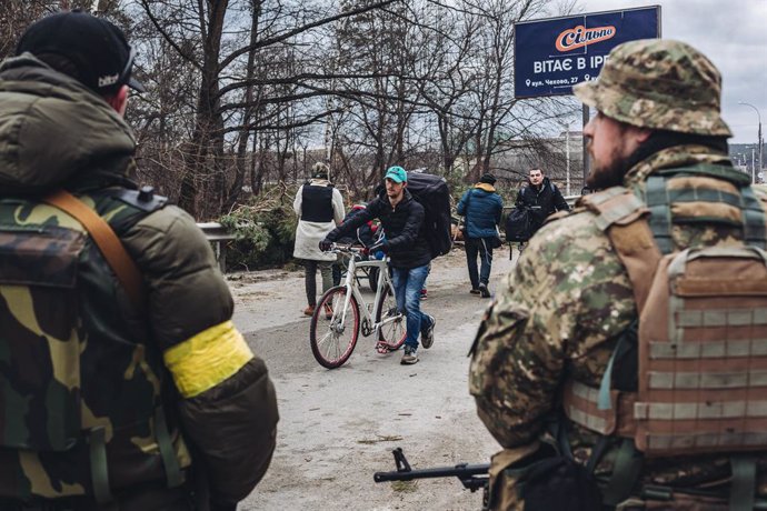 Un joven camina, junto a su bici, mientras dos soldados ucranianos le observan, a 5 de marzo de 2022, en Irpin (Ucrania). El ejército de Ucrania resiste por el momento el duro asedio de Rusia a su capital, Kiev, donde se recrudecen los combates. Nacione