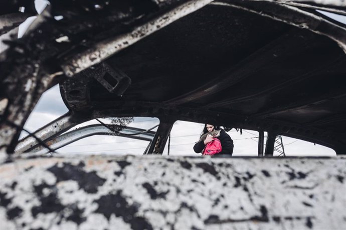 Una joven y su gato caminan frente a un coche calcinado, a 7 de marzo de 2022, en Irpin (Ucrania)