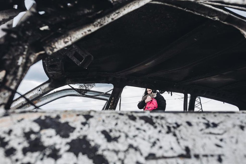 Una joven y su gato caminan frente a un coche calcinado, a 7 de marzo de 2022, en Irpin (Ucrania)