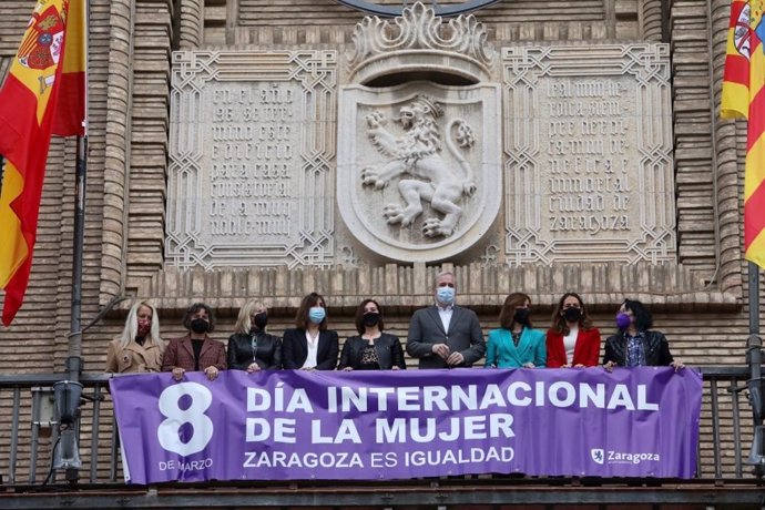 Representantes de los diferentes grupos municipales colocan la pancarta en el balcón del Ayuntamiento de Zaragoza.
