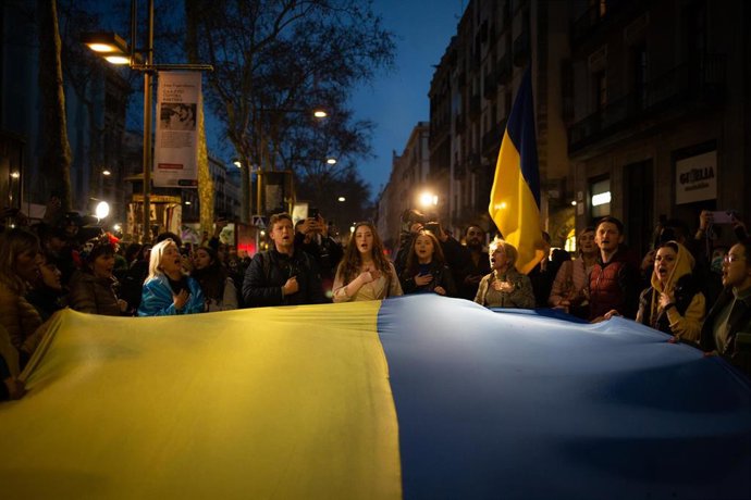 Un grupo de personas sostiene la bandera de Ucrania en una concentración bajando La Rambla desde la Plaza de Cataluña tras los primeros ataques rusos registrados en Ucrania esta pasada madrugada, a 24 de febrero de 2022, en Barcelona, Cataluña (España). 
