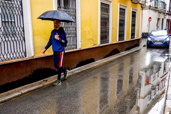 Un transeúnte, con paraguas en la mano,  por una estrecha calle céntrica de Sevilla, en una mañana donde la lluvia ha hecho acto de presencia en la capital a 08 de marzo del 2022 en Sevilla (Andalucía, España)