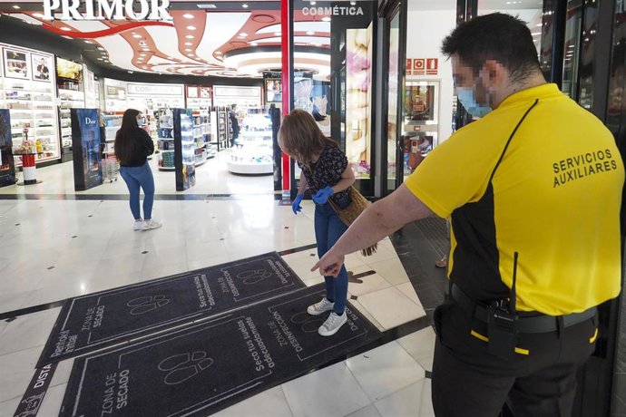Archivo - Un vigilante de seguridad le indica a una mujer cómo desinfectar su calzado en la entrada del Centro comercial Vallsur 
