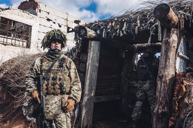 Un soldado del ejército ucraniano observa mientras otro apunta con su arma desde la trinchera en la línea del frente.