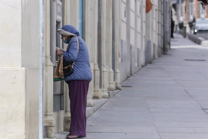 Archivo - Una mujer protegida con mascarilla y abrigada saca dinero de un cajero de Madrid, a 15 de abril de 2020.