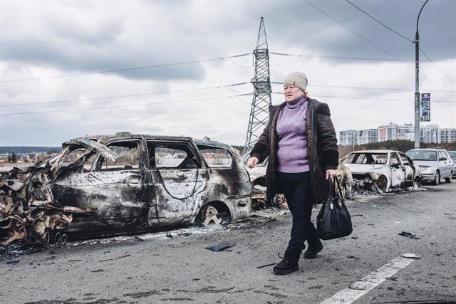 Una mujer junto a los restos de un coche quemado en Irpin, cerca de Kiev