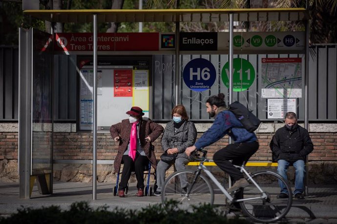 Una persona, en bicicleta, pasa junto a una parada, donde varias personas esperan el autobús, durante la huelga de autobuses en Mitre Ganduxer, a 17 de febrero de 2022, en Barcelona, Cataluña, (España). Los sindicatos CCOO, UGT, ACTUB, SIT, CGT y ACAT h