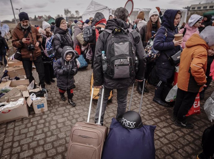 05 March 2022, Poland, Medyka: A journalist with a hard hat in his luggage walks past refugees at the Ukrainian-Polish border. More than a milion people have fled Ukraine to the neighbouring countries due to the Russian invasion. Photo: Kay Nietfeld/dpa