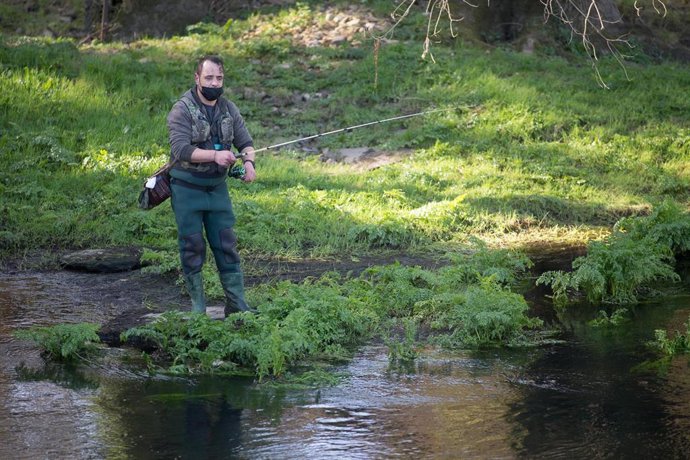 Archivo - Un pescador sostiene con su caña una trucha capturada.