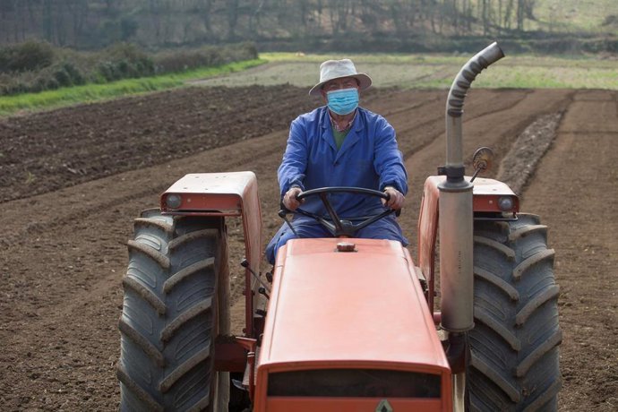 Archivo - Un agricultor ara sus fincas con el tractor y la mascarilla (archivo)