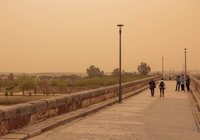 Peatones en el Puente Romano de Mérida bajo la calima.