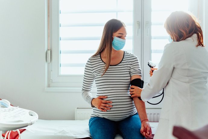 Archivo - Médico con una mujer embarazada usando máscaras médicas durante un examen.