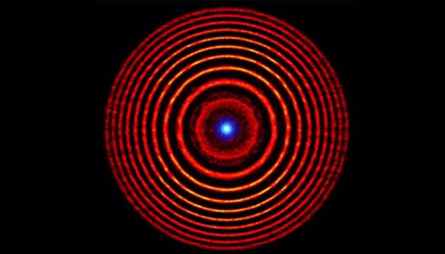 Ilustración coloreada de una simulación de una lente de plasma holográfica. Los círculos concéntricos rojos indican alternancia de anillos de plasma de alta y baja densidad. El punto azul en el centro representa la luz enfocada.