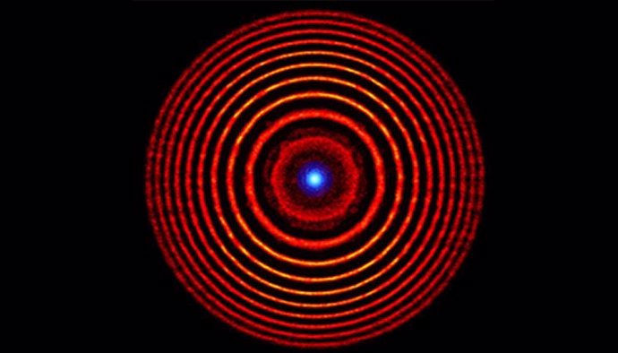 Ilustración coloreada de una simulación de una lente de plasma holográfica. Los círculos concéntricos rojos indican alternancia de anillos de plasma de alta y baja densidad. El punto azul en el centro representa la luz enfocada.