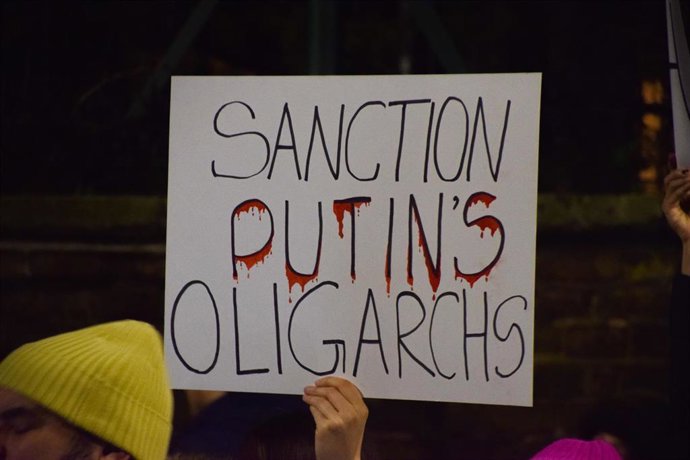 Un manifestante sostiene una pancarta con el lema 'Sancionar a los oligarcas de Putin' en una protesta por la invasión rusa de Ucrania.