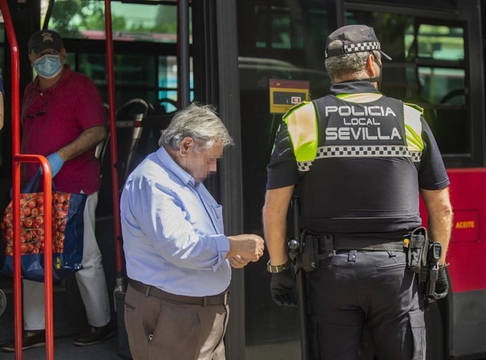Archivo - Un agente de la policía local pide la identificación a un pasajero tras bajarse de un autobús sin mascarilla, en foto de archivo. 