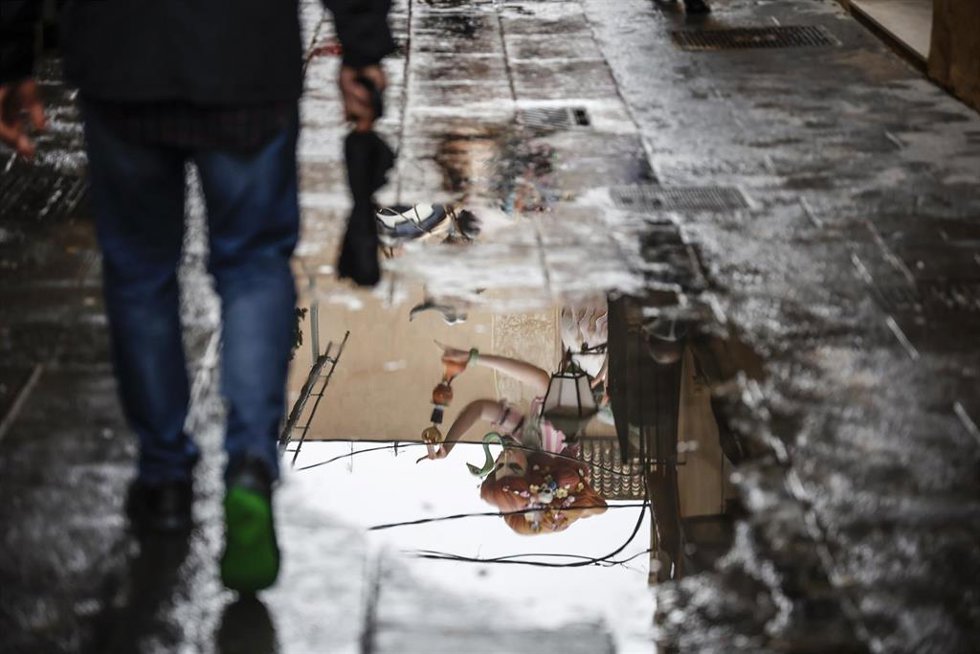 Una persona, con un paraguas, pasea por encima de un charco donde se refleja una falla, a 17 de marzo de 2022, en Valencia Comunidad Valenciana, (España).