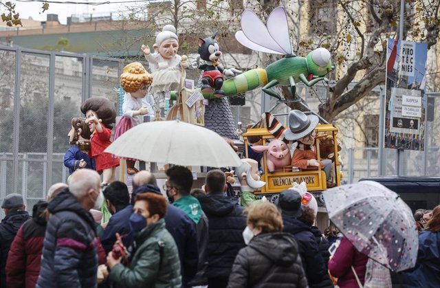 Varias personas con paraguas pasan por delante de la falla infantil del Ayuntamiento de València. 