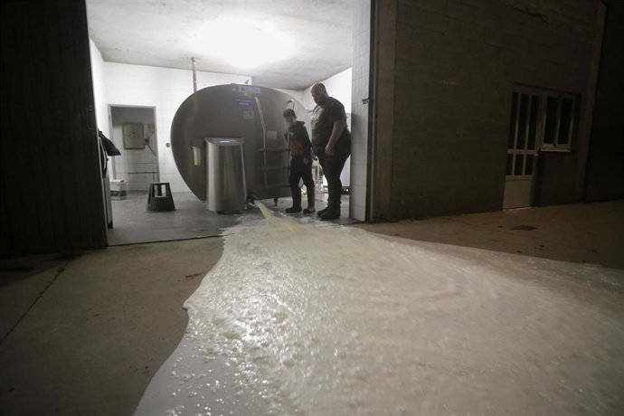 Un ganadero y un niño vierten la leche al suelo después de que la industria láctea tenga que parar su actividad a partir de hoy, a 17 de marzo de 2022, en Vilela, Outeiro de Rei, Lugo, Galicia (España). La industria láctea para su actividad al no poder 