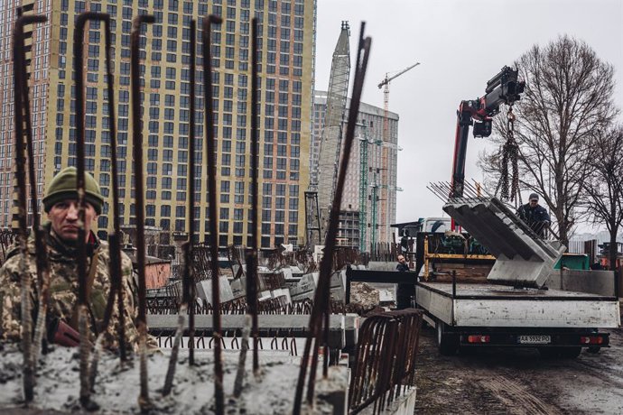 Varios operarios cargan losas de cemento frente a un miliciano ucraniano, a 2 de marzo de 2022, en Kiev (Ucrania). Las autoridades de Kiev han declarado el toque de queda en la ciudad ante la situación causada por la ofensiva rusa en el país. Más de 2.0
