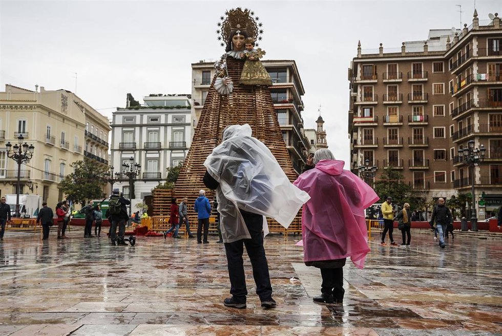Dos personas con chubasqueros delante de la Virgen de los Desamparados, antes de celebrarse la ofrenda floral