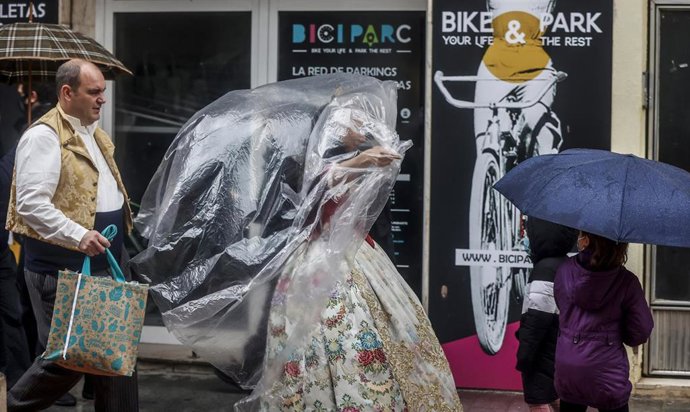 Una fallera se cubre con un plástico de camino a la ofrenda floral a la Virgen de los Desamparados, a 17 de marzo de 2022, en Valencia, Comunidad Valenciana (España). La Junta Central Fallera ha decidido celebrar el desfile de esta tarde, pese al tempor