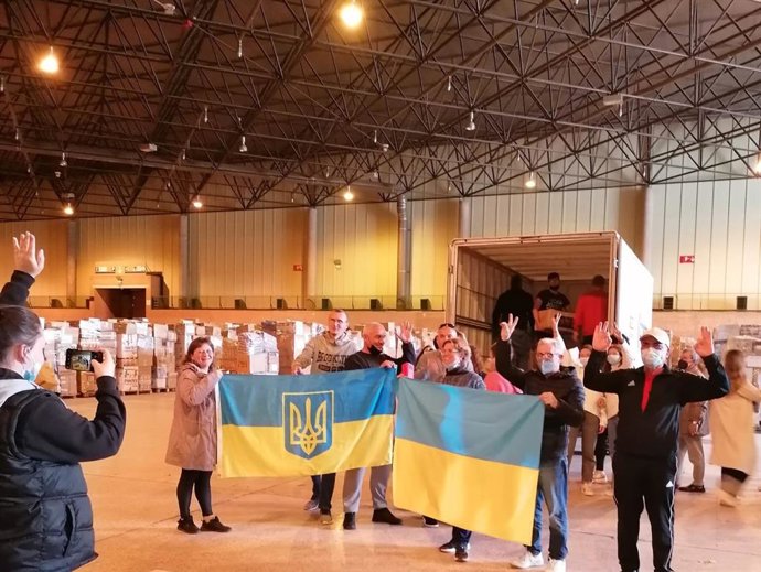 Voluntarios portan banderas de Ucrania tras cargar un camión con ayuda humanitaria.