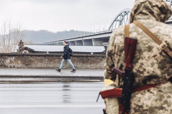 Un civil camina frente a un miliciano ucraniano por una calle de Kiev, a 2 de marzo de 2022, en Kiev (Ucrania). Las autoridades de Kiev han declarado el toque de queda en la ciudad ante la situación causada por la ofensiva rusa en el país. Más de 2.000 
