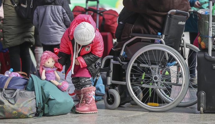 21 March 2022, Saxony, Leipzig: A Ukrainian girl plays next to a group of refugees from Ukraine and a senior citizen in a wheelchair at the main train station in Leipzig. Photo: Jan Woitas/dpa-Zentralbild/dpa