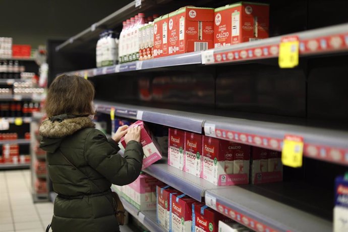 Una mujer coge un brick de leche de la estantería de leche que le faltan algunos productos, en una imagen de archivo.