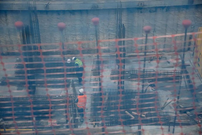 Vista de dos obreros, trabajando en el forjado de una obra, a través de una red de seguridad, en unos edificios en construcción, en Vallecas
