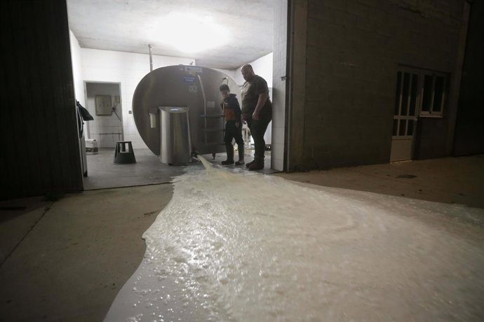 Un ganadero y un niño vierten la leche al suelo después de que la industria láctea tenga que parar su actividad a partir de hoy, a 17 de marzo de 2022, en Vilela, Outeiro de Rei, Lugo, Galicia (España). La industria láctea para su actividad al no poder 