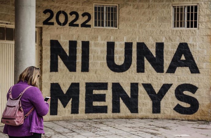 Una mujer pasa por delante de una pared donde se puede leer "Ni una menos" en un acto en memoria de las víctimas de violencia de género, en Valencia.