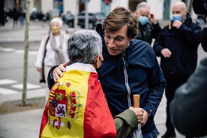 El alcalde de Madrid, José Luis Martínez-Almeida, saluda a una mujer cubierta con una bandera de España en una manifestación a favor de las víctimas del terrorismo, en la Plaza de Colón.