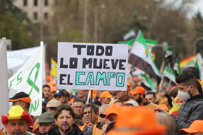 Varios manifestantes, con gorras naranjas con una pancarta que reza 'Todo lo mueve el campo', durante la  la marcha por el mundo rural 20M, a 20 de marzo de 2022, en Madrid (España). Los organizadores de esta convocatoria, denominada como 20M,  son 